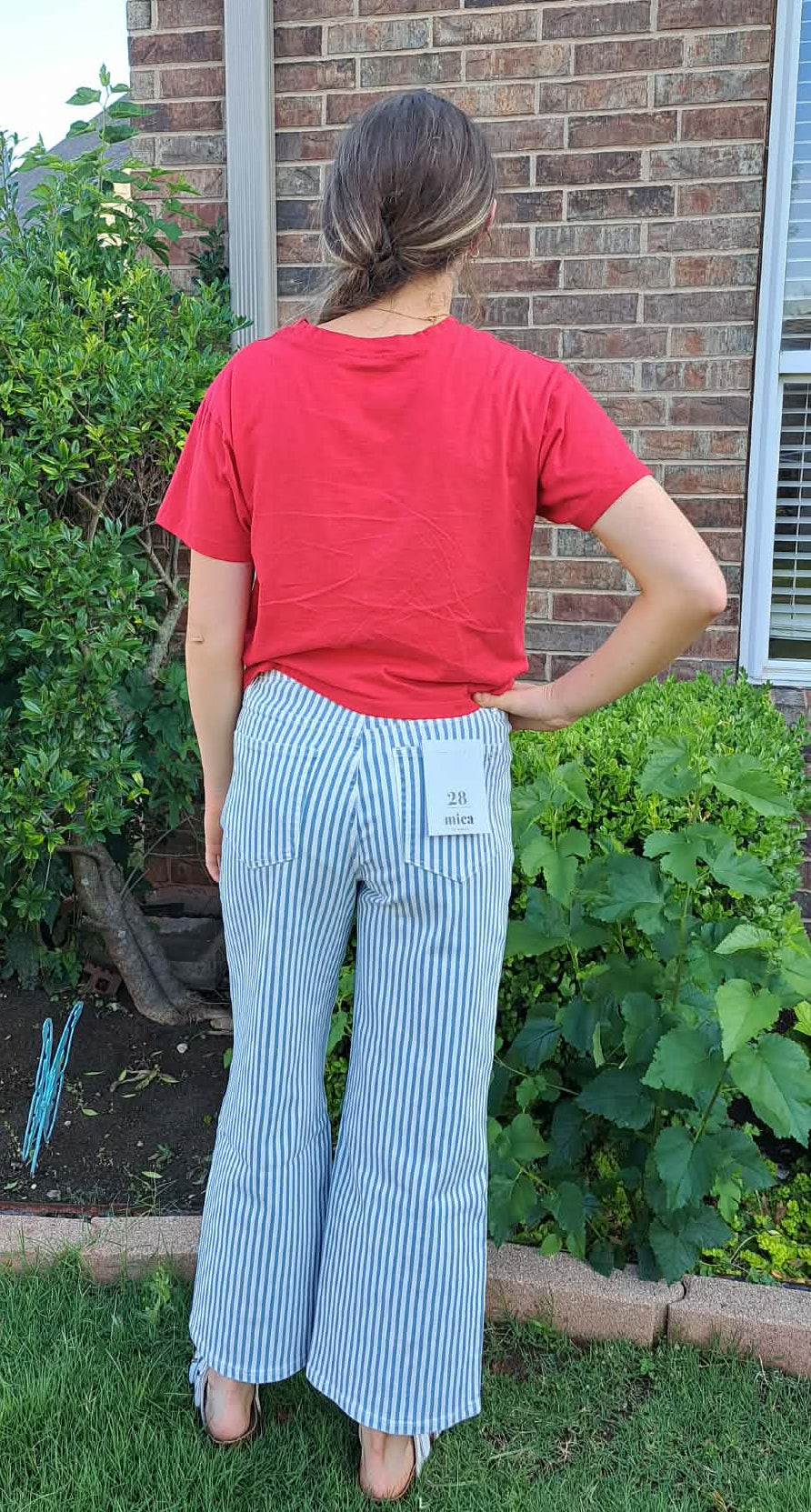 Person wearing a red shirt and light blue striped pants standing in a garden.