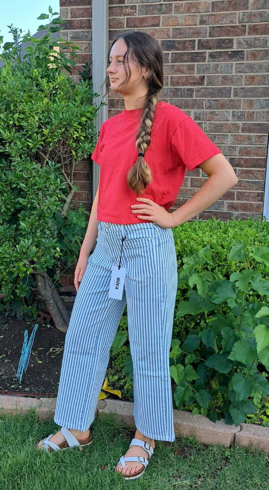 Person wearing a red shirt and light blue striped pants standing in a garden.