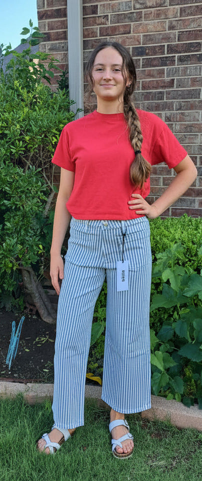 Person wearing a red shirt and blue striped pants standing in front of a brick house.