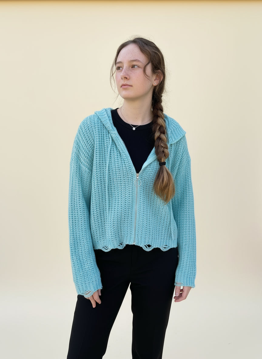 Person wearing a light blue sweater over a black top and black pants. Cream background