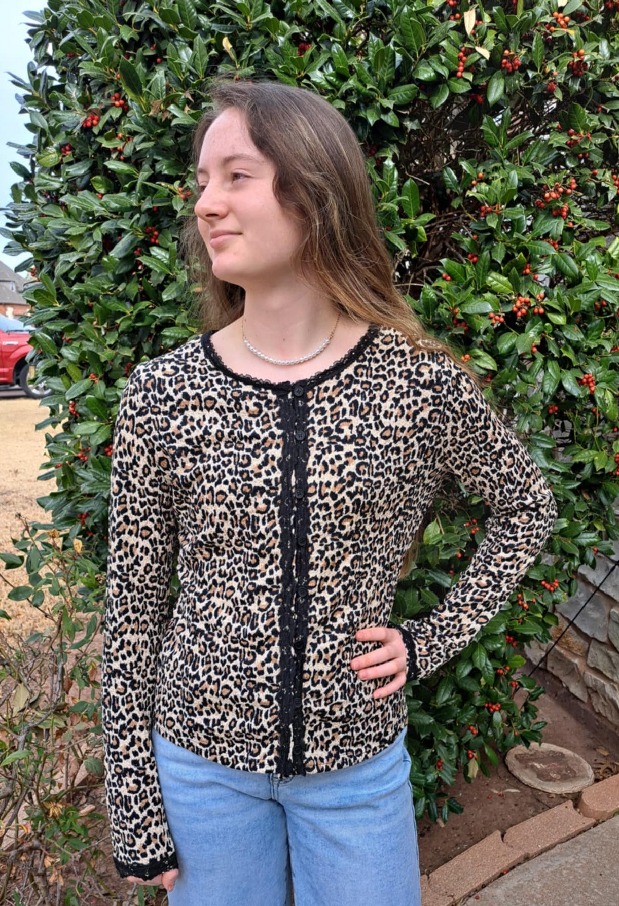 Person wearing a leopard print top and blue jeans standing in front of a stone wall and greenery.