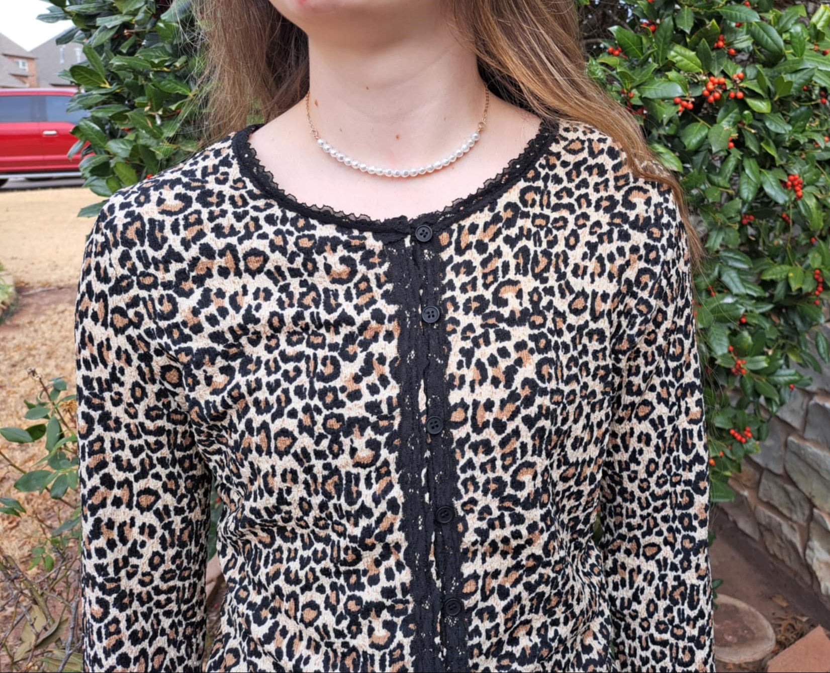 Person wearing a leopard print top with a stone wall and greenery in the background