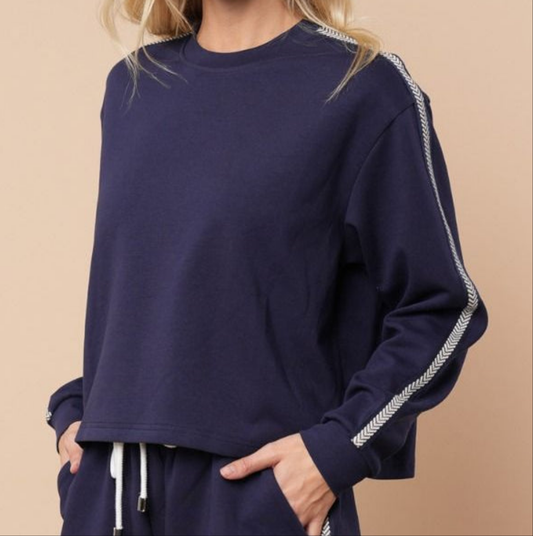 Navy long sleeve knit top with white accent stripe on a person. Beige background