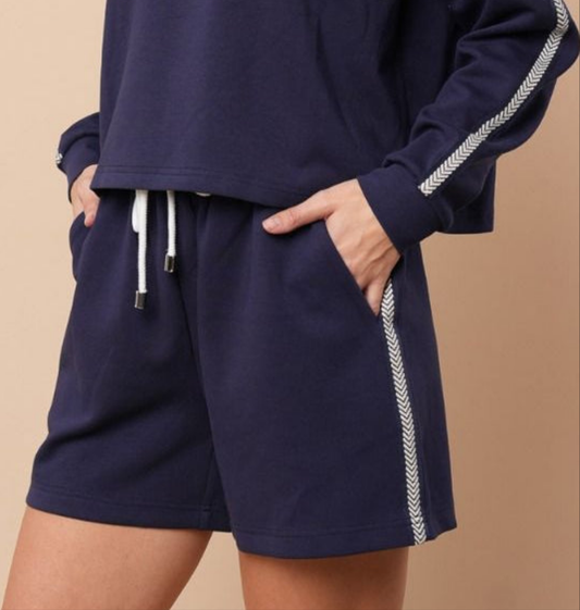 Navy knit shorts with white arrow stripe down the side on a beige background