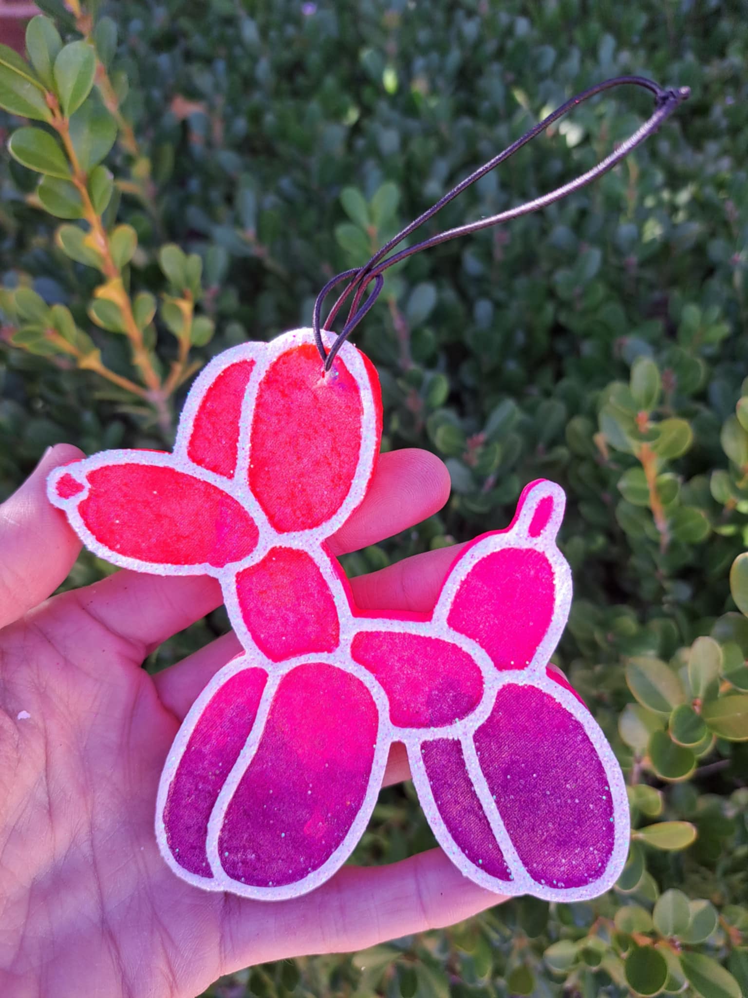 Pink ombre balloon dog freshie held in a hand with a green leafy background