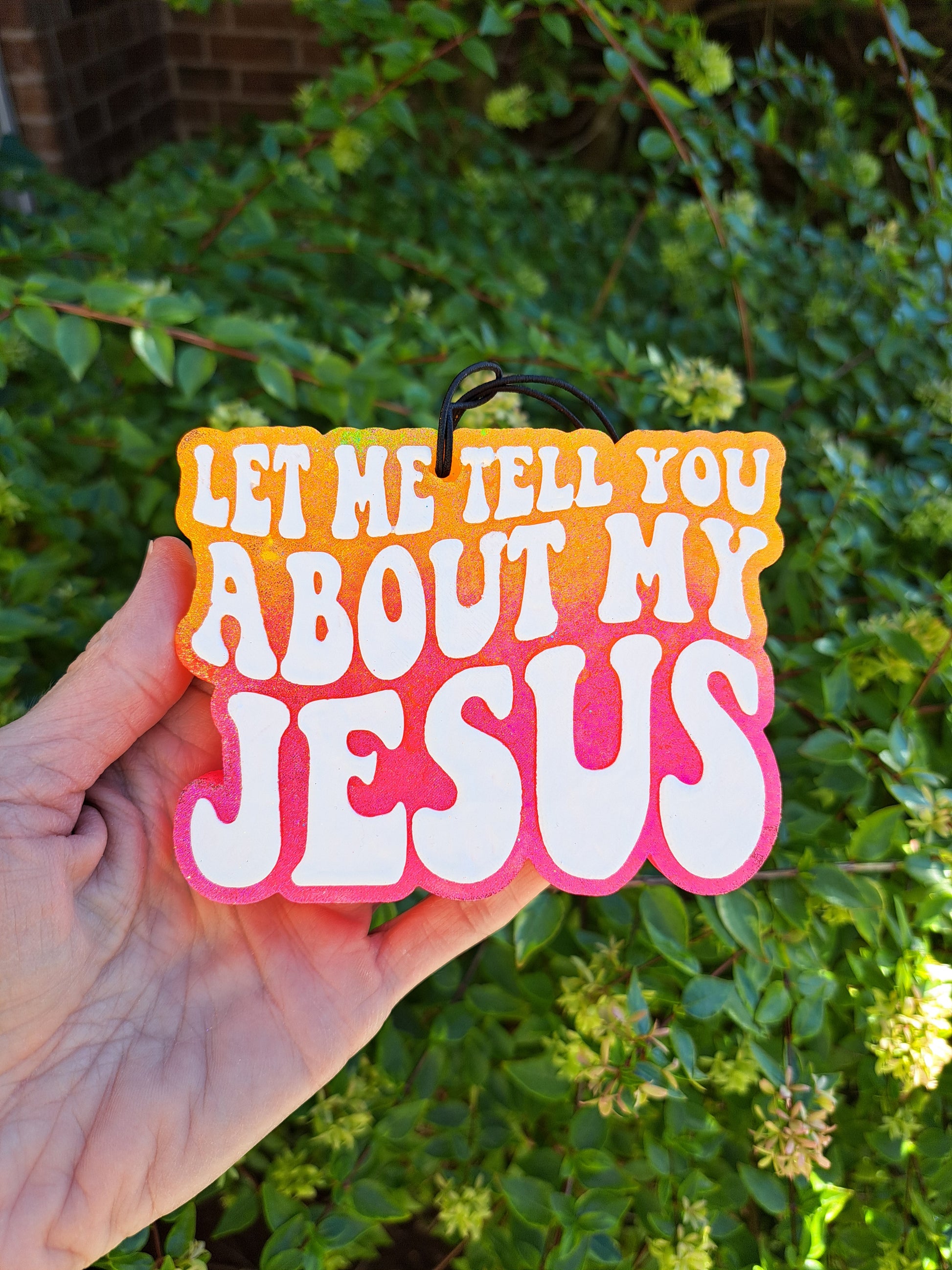 A hand holding a an ombre air freshener with white text that says 'LET ME TELL YOU ABOUT MY JESUS' written on it.