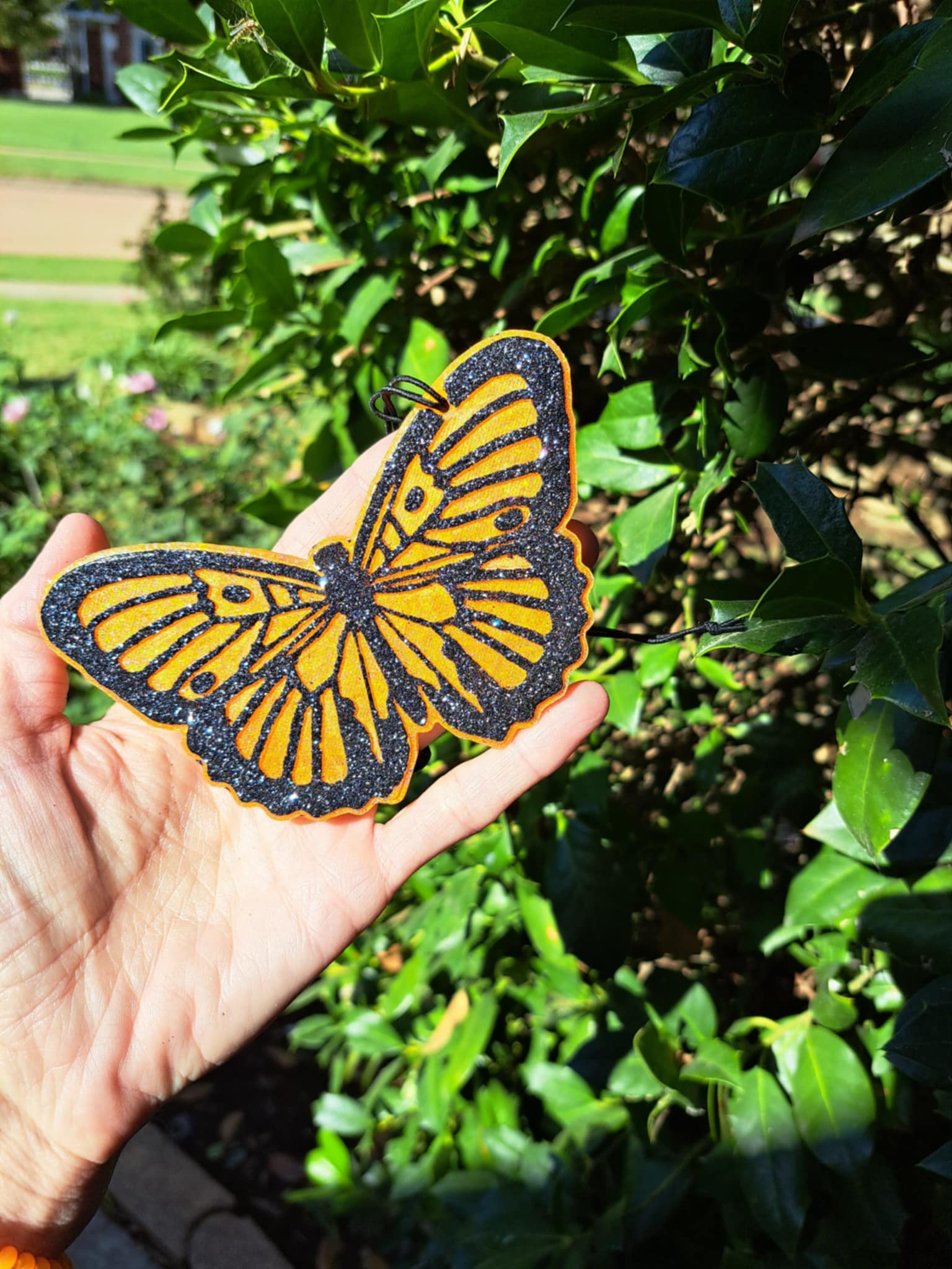 orange butterfly air freshener held in a hand with greenery background
