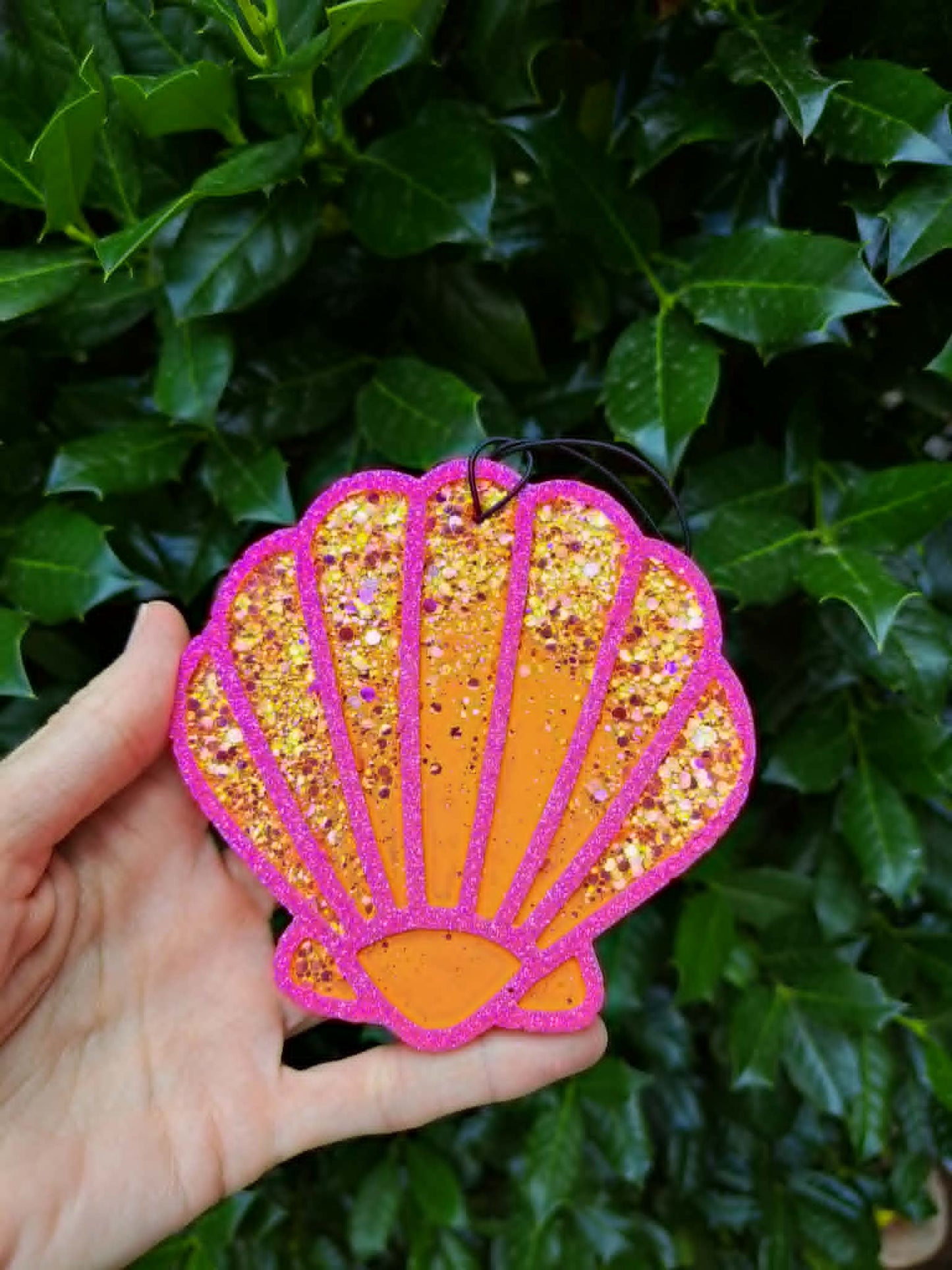 Hand holding a glittery shell-shaped freshie against a green leafy background