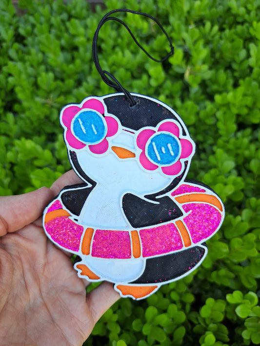 Colorful penguin air freshener held against a green leafy background
