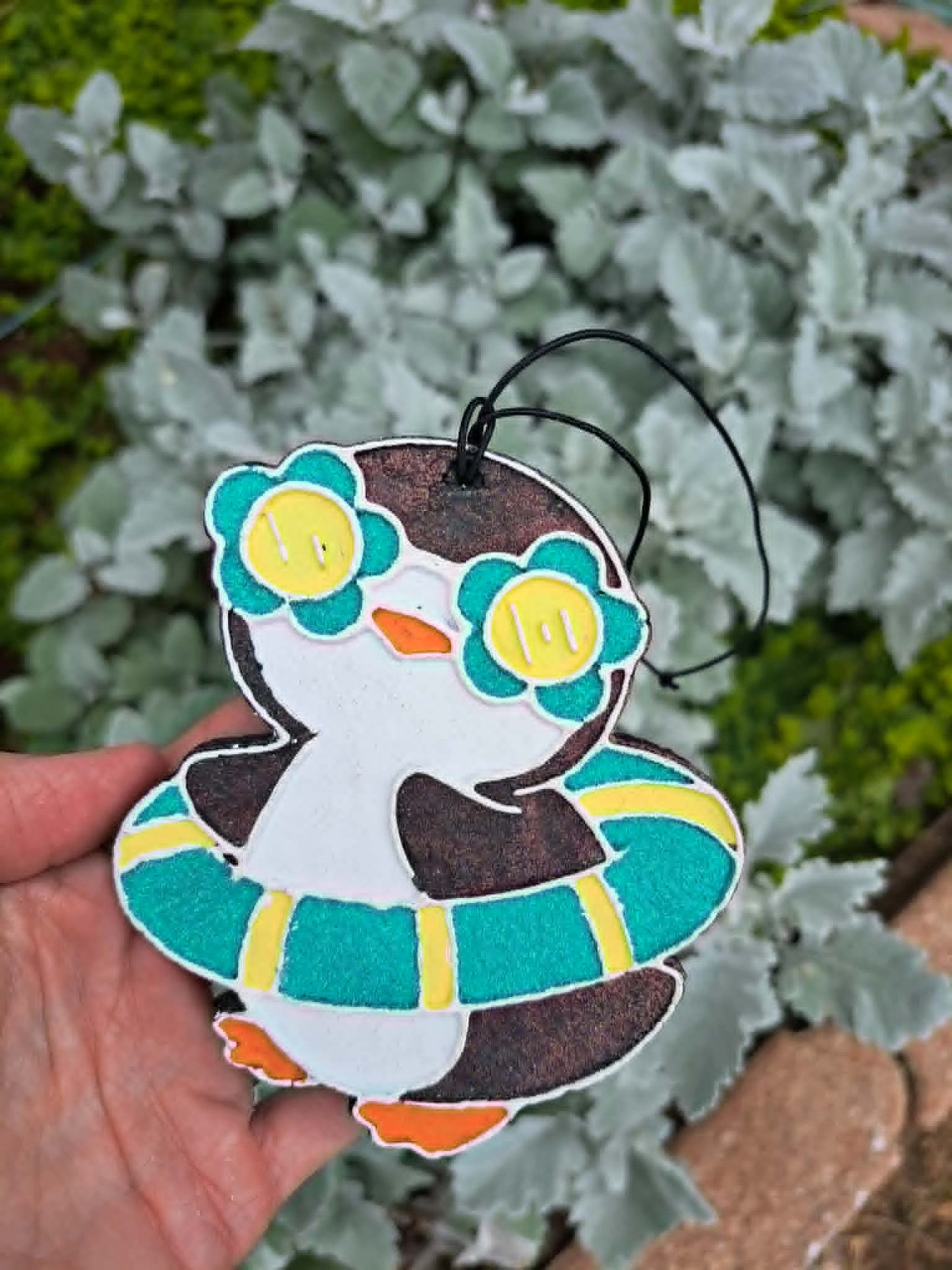 Decorative penguin freshie in glasses with held in front of greenery.