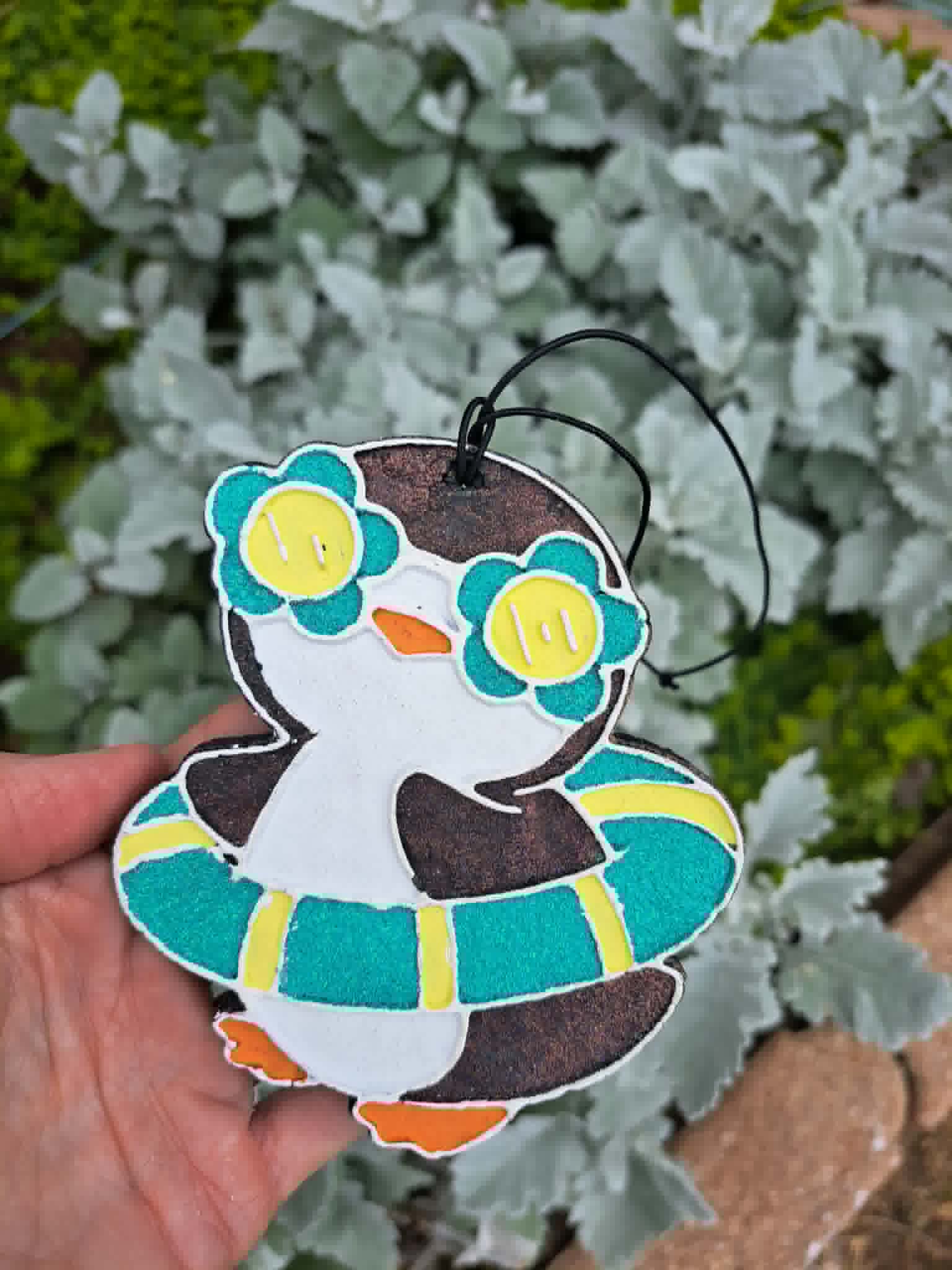 Decorative penguin freshie in glasses with held in front of greenery.