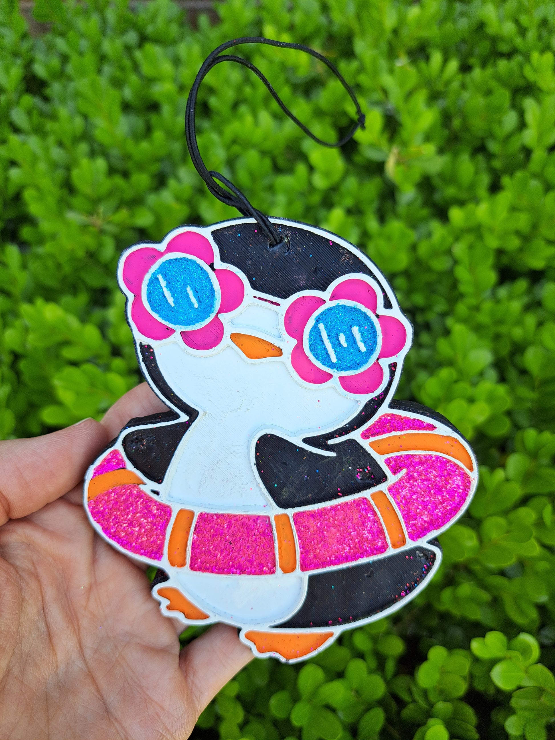 Penguin air freshener held in hand against leafy background