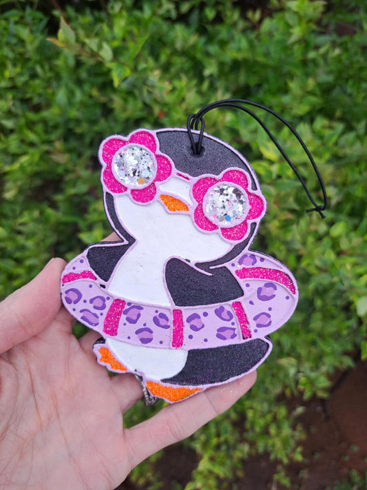 Handmade and painted hanging air freshener in the shape of a penguin with pink leopard print design, featuring rhinestone eyes, on a black elastic string.