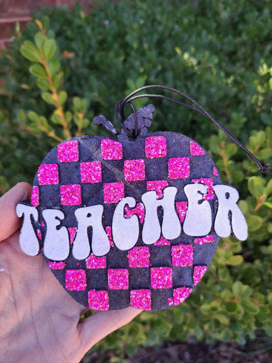 Heart-shaped freshie with 'TEACHER' text on a checkered pattern against a blurred green background