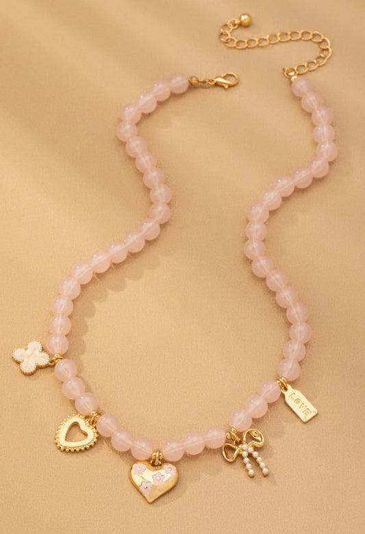 Necklace with pink beads and gold charms on a beige background