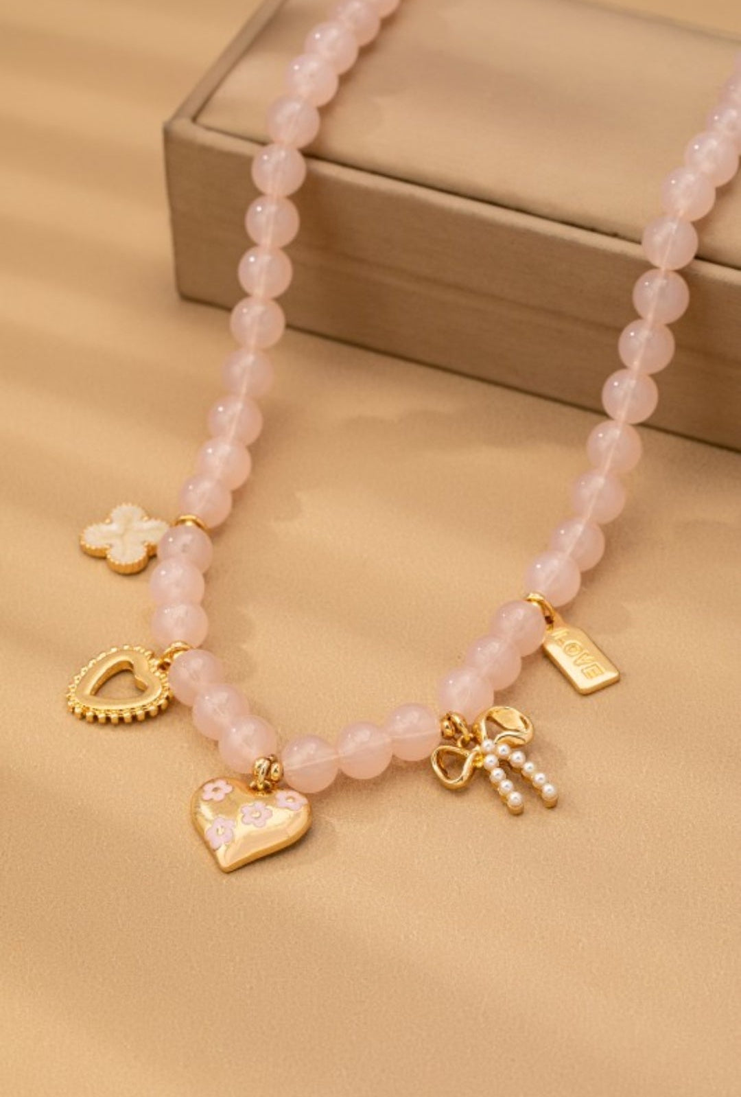 Pink beaded necklace with gold charms on a beige surface