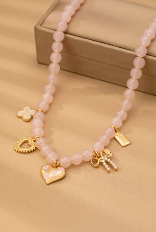 Pink beaded necklace with gold charms on a beige surface