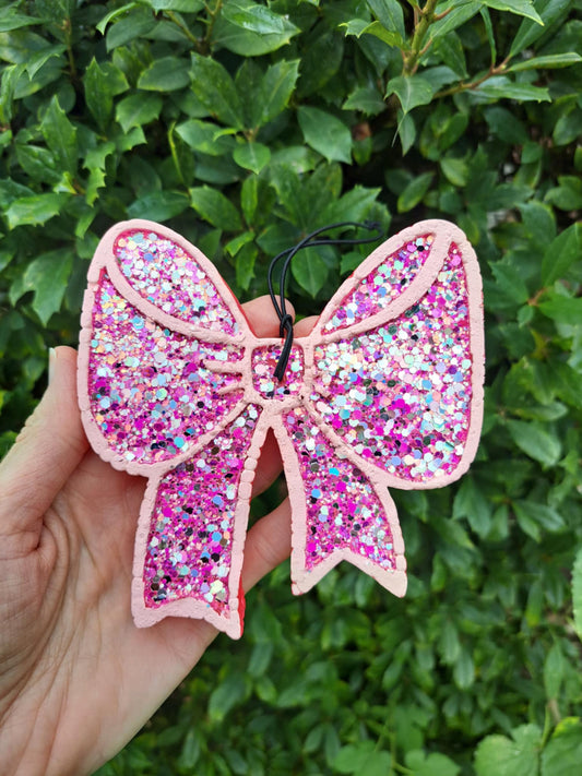 chunky glitter bow air freshener held in a hand on a green background