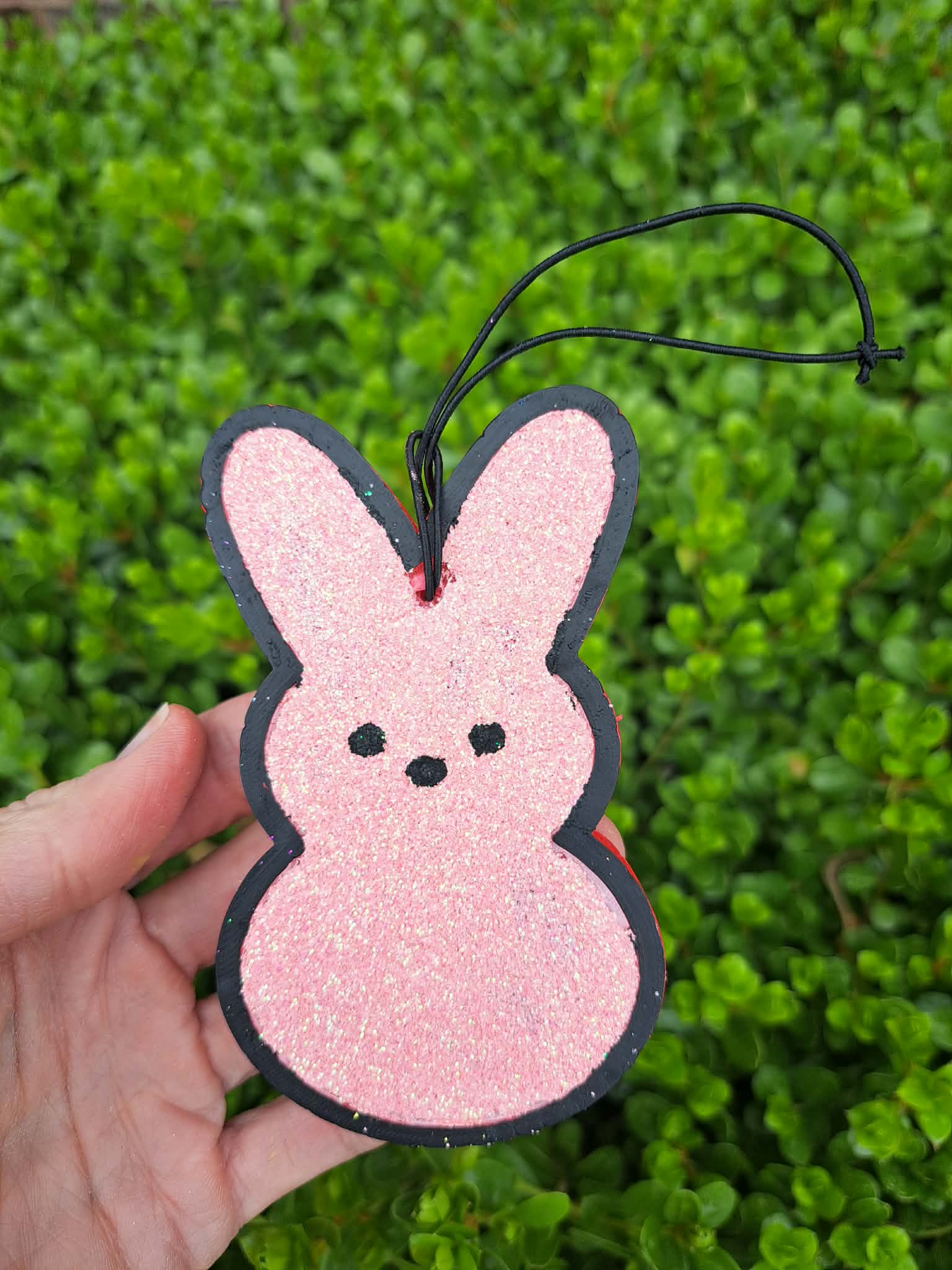 Pink glittery bunny-shaped freshie held in front of green foliage