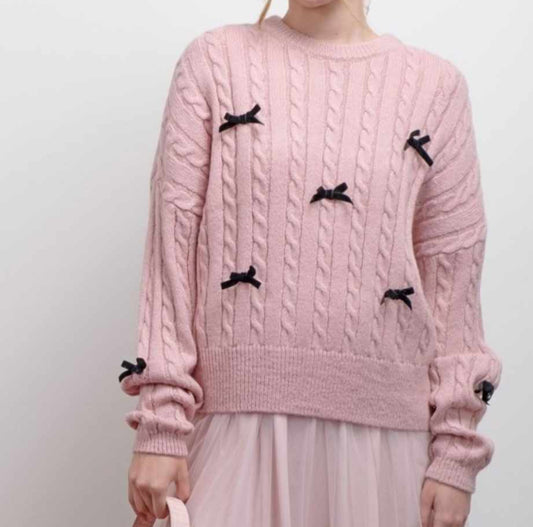 person wearing a pink cable knit sweater with black bows on a white background
