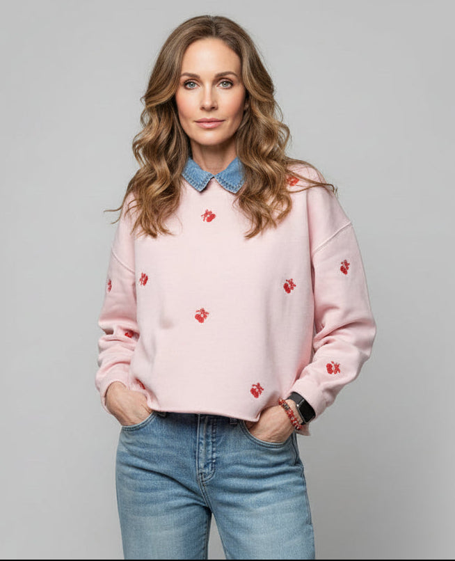 Woman wearing a pink sweater with red patterns and blue jeans on a gray background