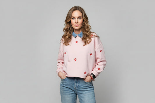 Woman wearing a pink sweater with red patterns and blue jeans on a gray background