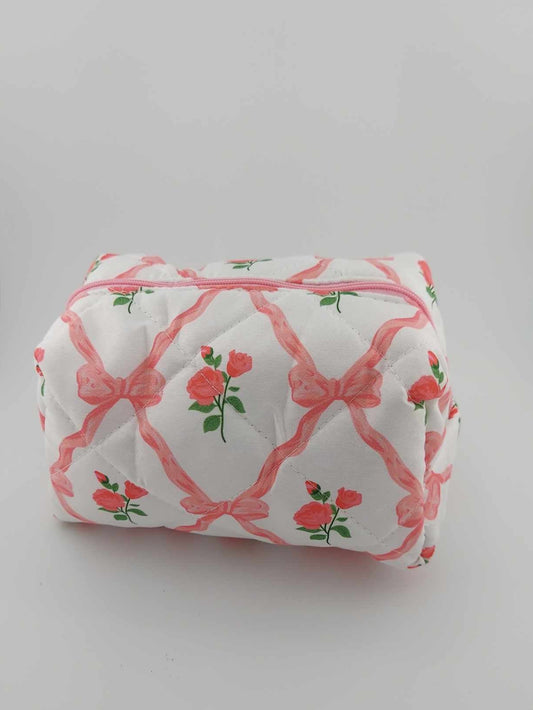 A pink cosmetic makeup pouch with a floral and bow pattern, displayed against a plain background.