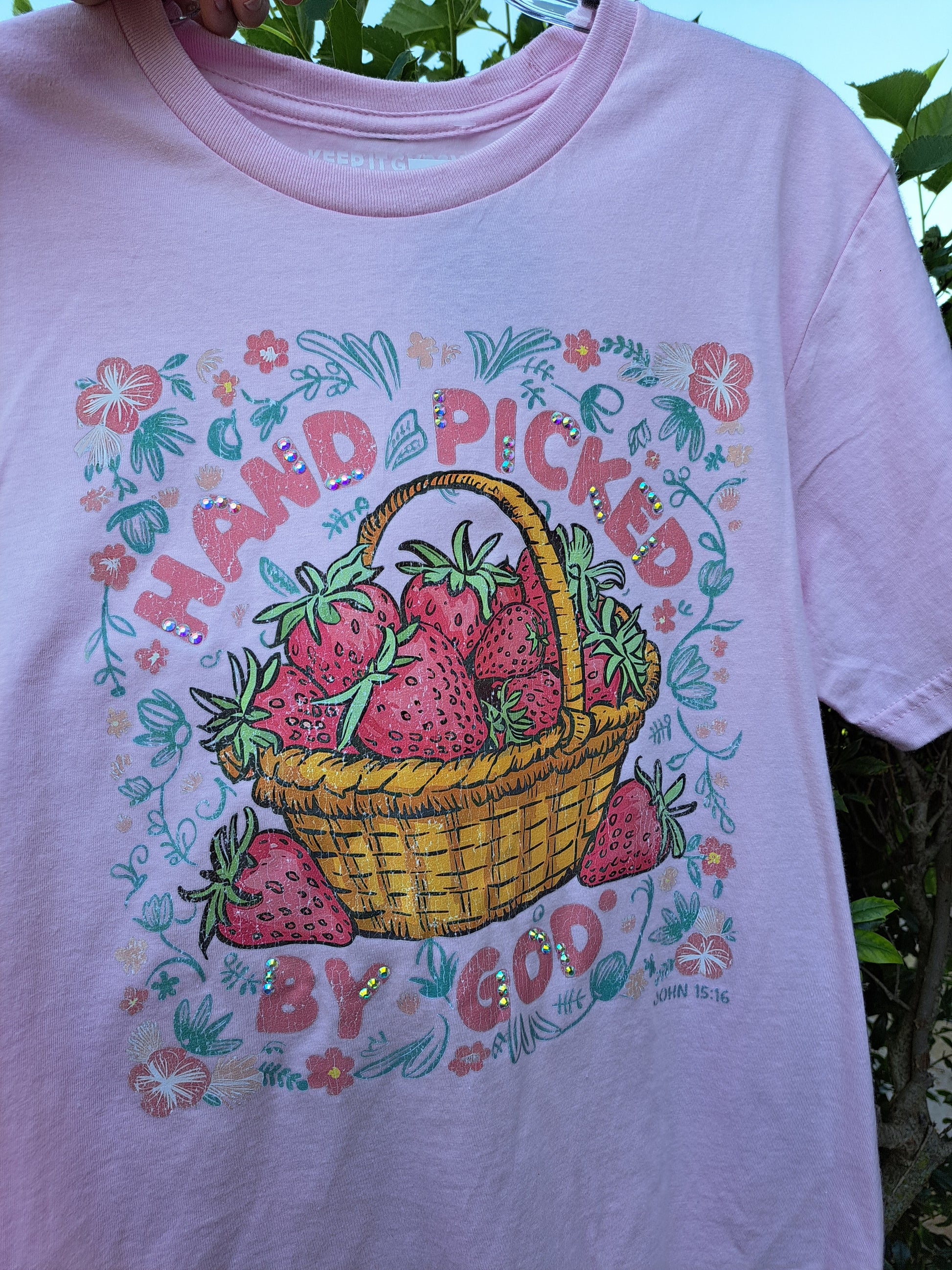 Pink t-shirt with a strawberry-themed design featuring a basket and text.