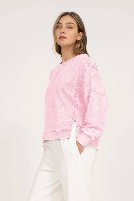 Side view of a woman wearing a pink tie-dye sweatshirt and white pants on a light gray background