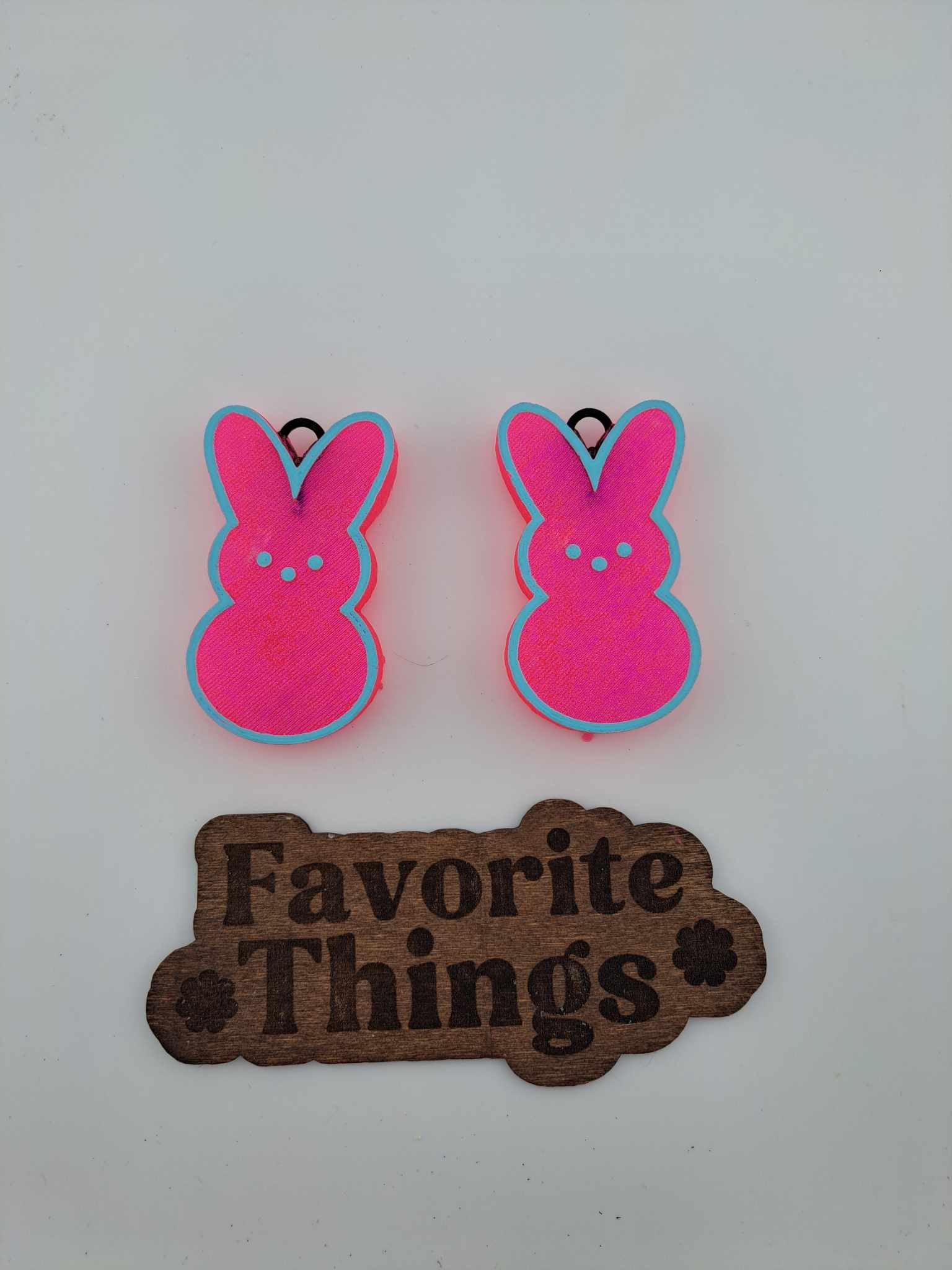 Two pink peep-shaped vent clips with blue trim, designed to look like rabbits, placed on a surface with a 'Favorite Things' wooden sign in the background.