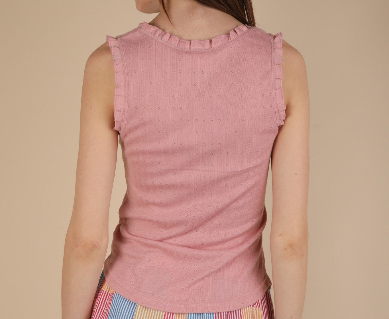 back view of a woman wearing a pink ruffle trim tank top against a beige background