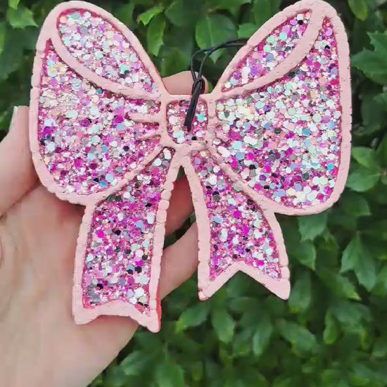 video of chunky glitter bow air freshener held in a hand with a green background