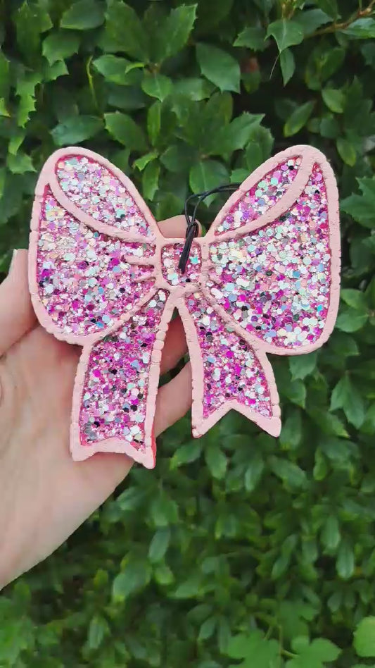 video of chunky glitter bow air freshener held in a hand with a green background