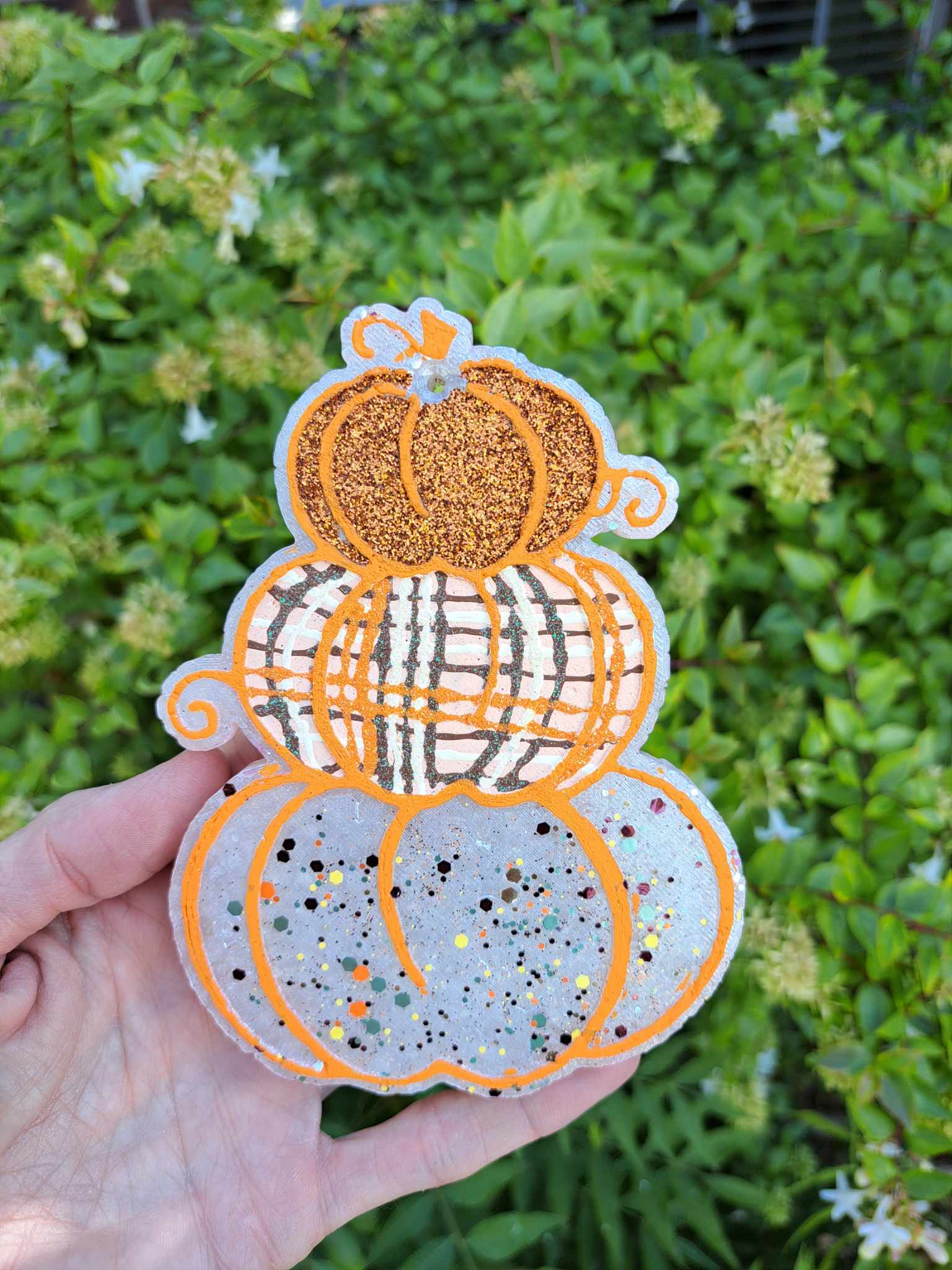 hand holding a freshie that looks like a stack of three pumpkins with the bottom one white, the center one painted plaid and the top one orange glitter
