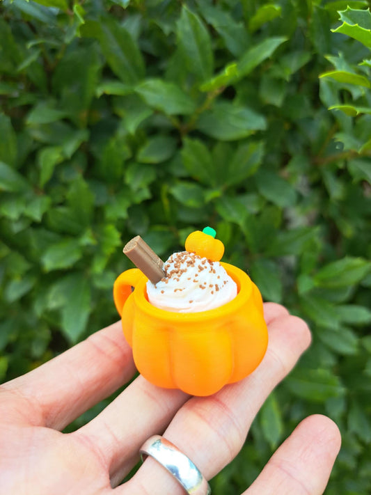 hand holding an orange pumpkin shaped 3D clicker against a greenery background