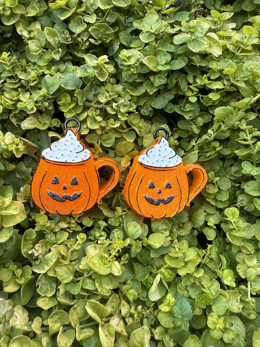 Pair of orange pumpkin-shaped vent clip freshies with black faces on a green leaf background