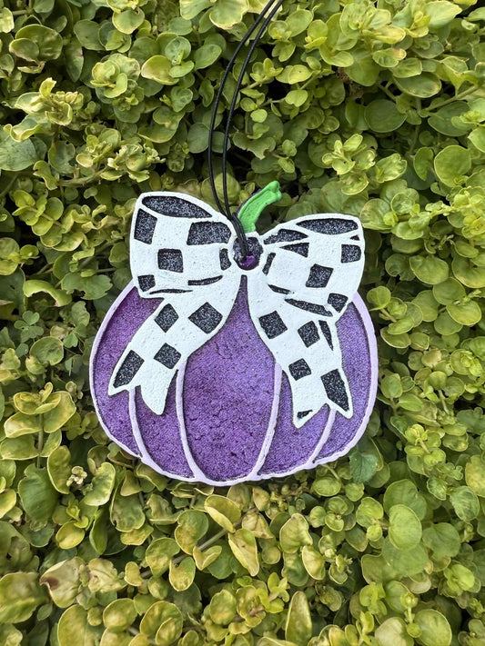 Purple pumpkin with black white checkered bow. Greenery background.