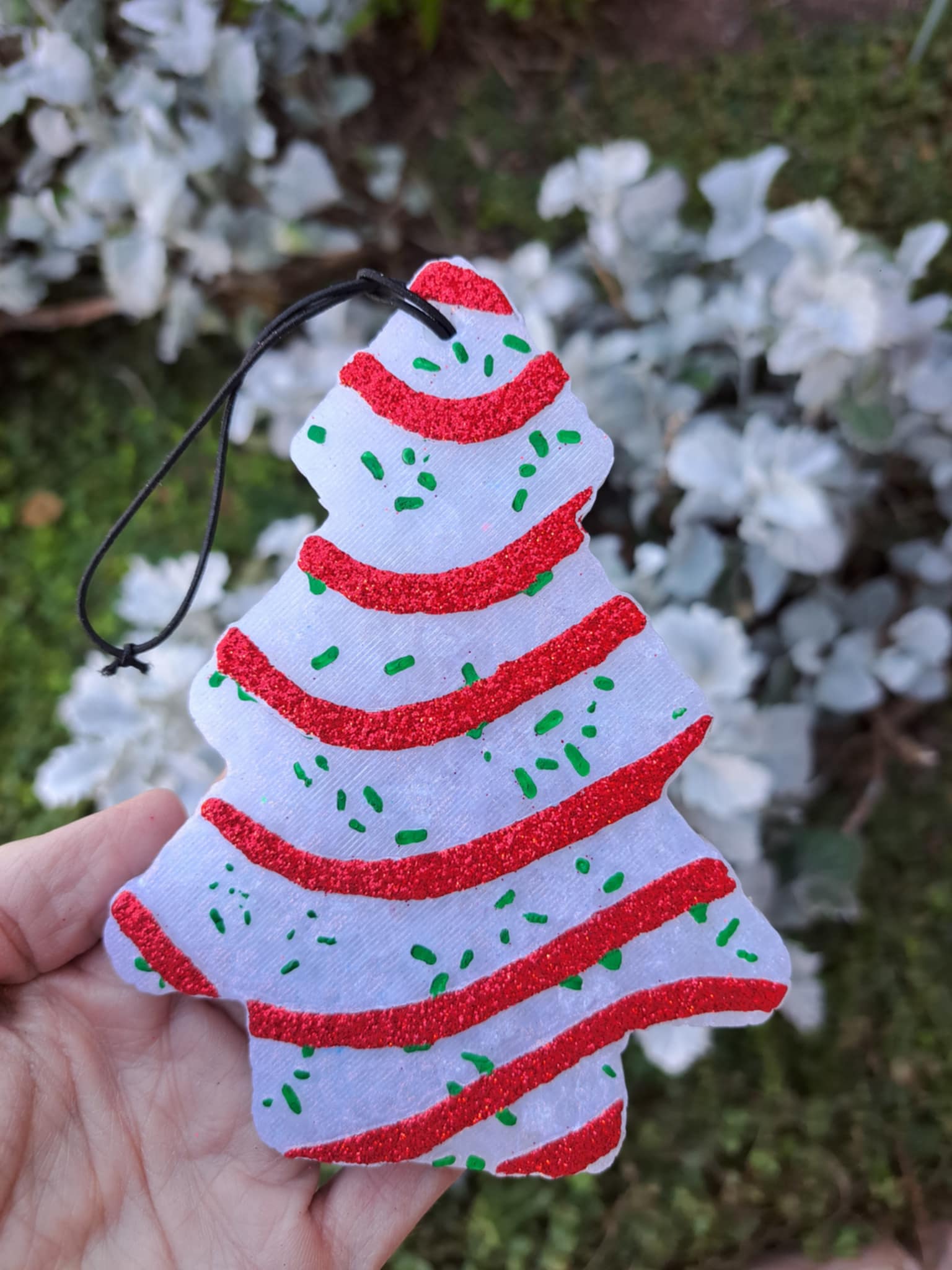 Decorative Christmas tree freshie with red and green stripes held by a hand against a blurred natural background.