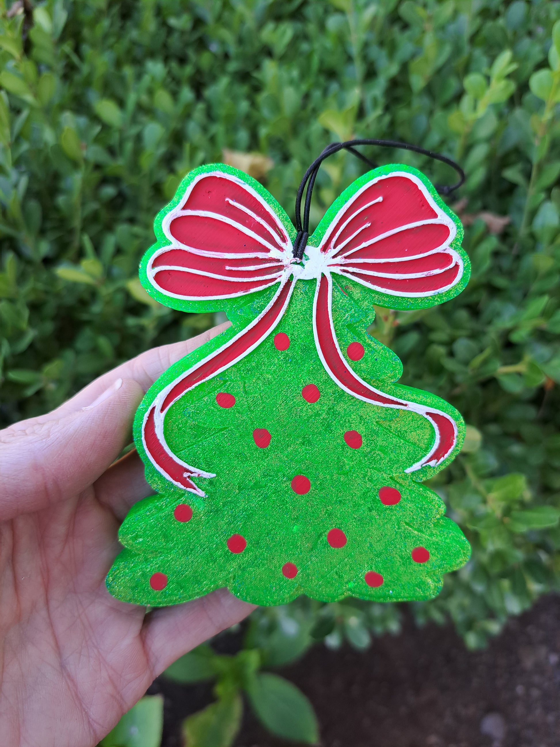 Green tree freshie with red bow and berries held in front of a shrub