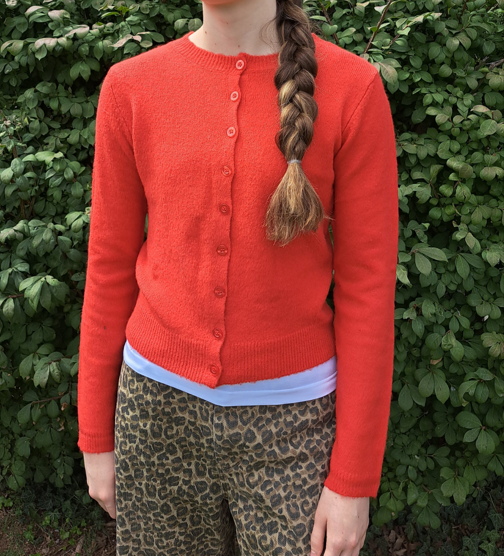 Person wearing a red cardigan with a green leafy background