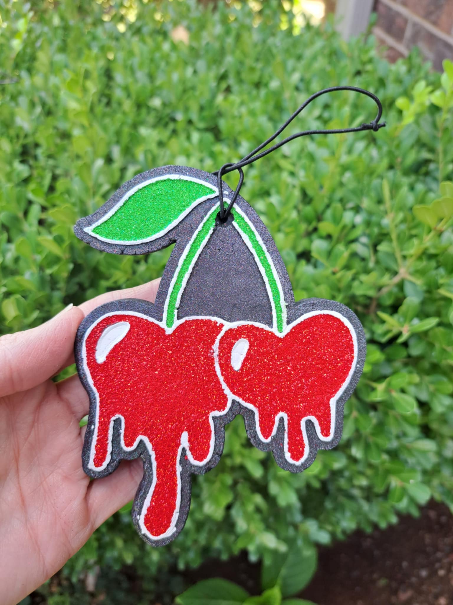 hand holding a red cherry drop freshie in front of greenery