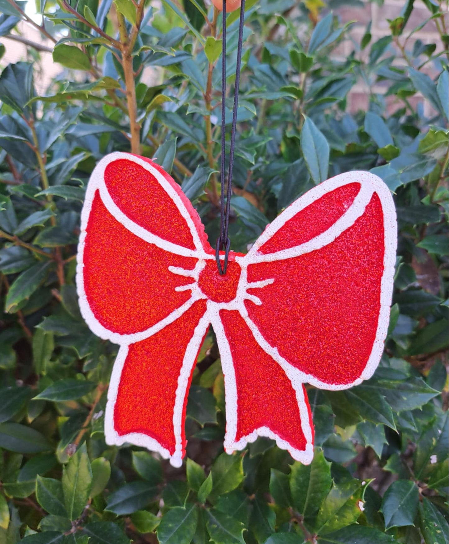 Red bow-shaped air freshener held against a green leafy background