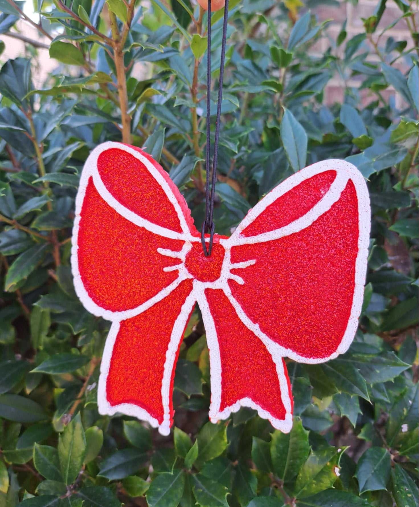 Red bow-shaped air freshener held against a green leafy background