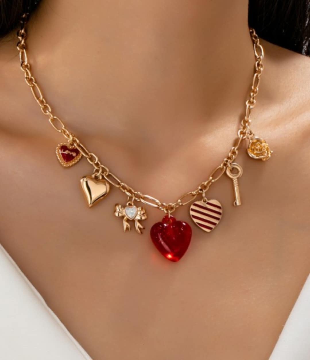 Gold necklace with various charms including a red heart, key, and others on a model.