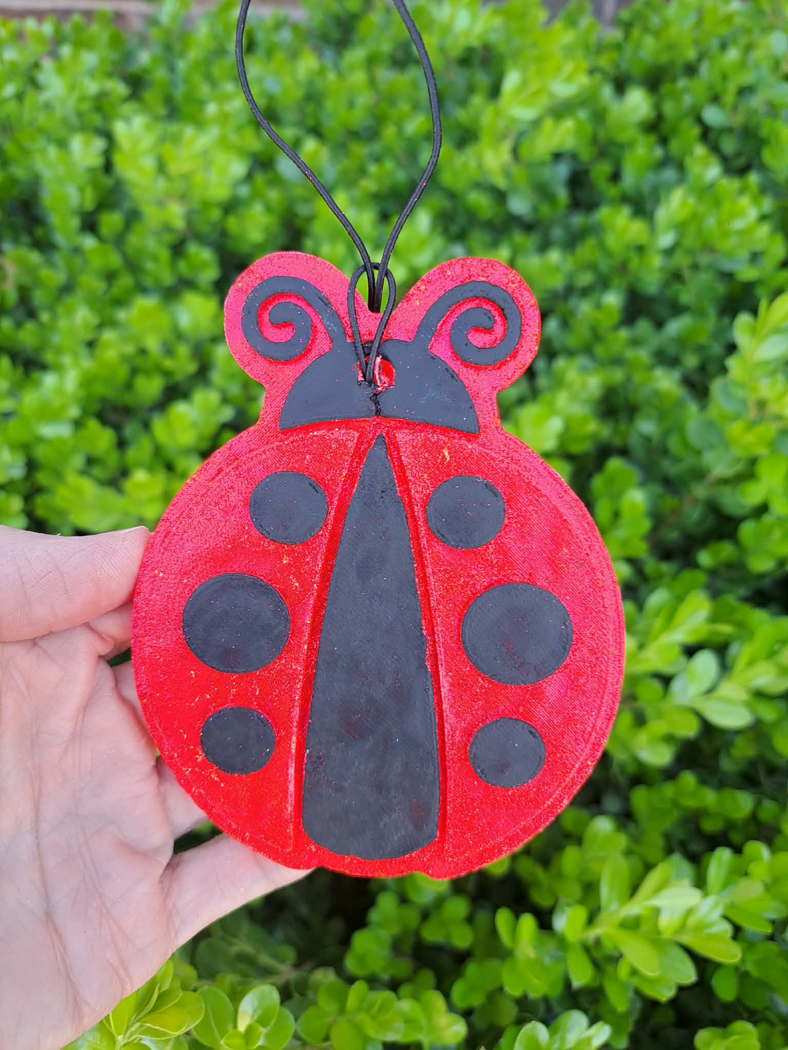 Red ladybug-shaped freshie held in front of green foliage