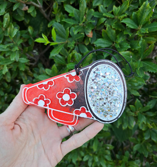Hand holding a megaphone freshie with red and silver designs against a green leafy background