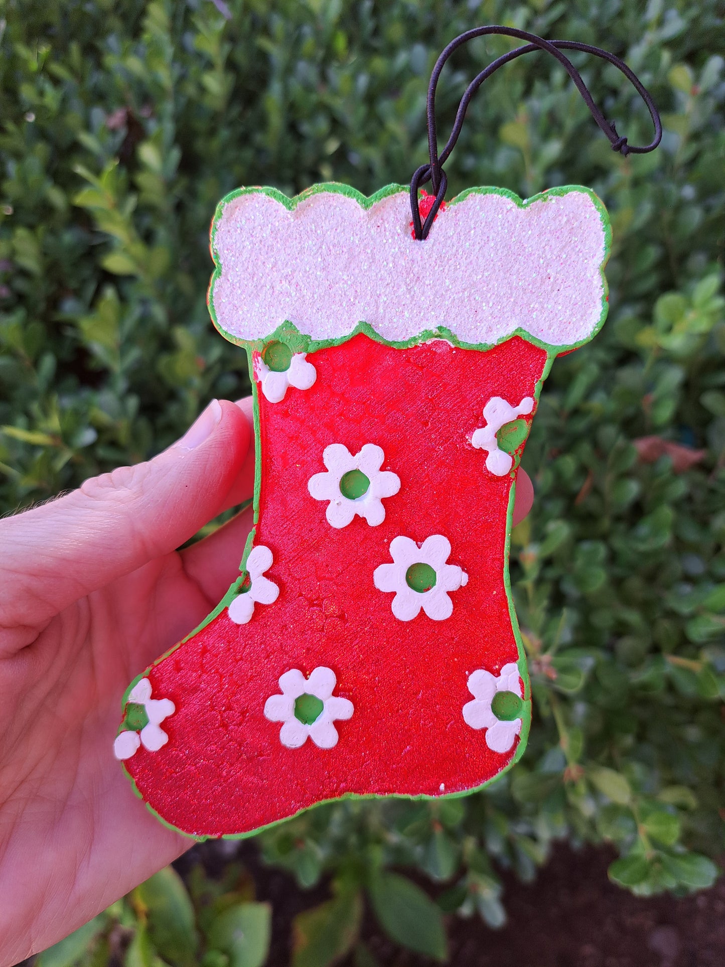 Red stocking freshie with green and white daisies held in front of shrub