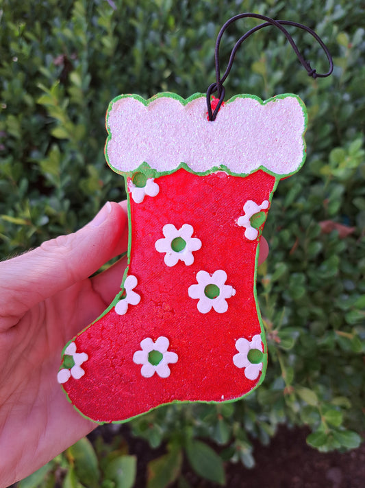 Red stocking freshie with green and white daisies held in front of shrub