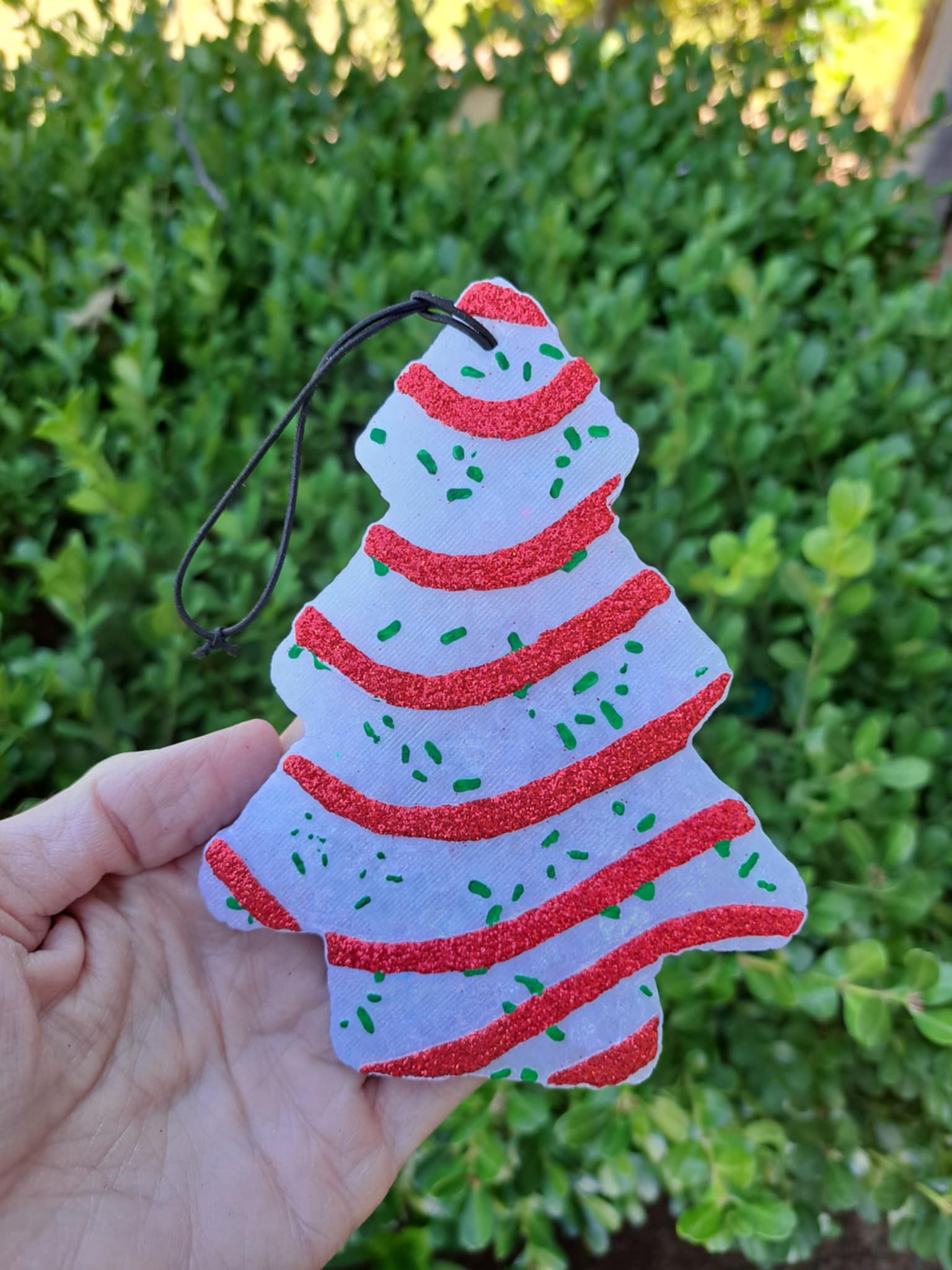 Decorative Christmas tree freshie with red and white stripes held in front of green foliage.