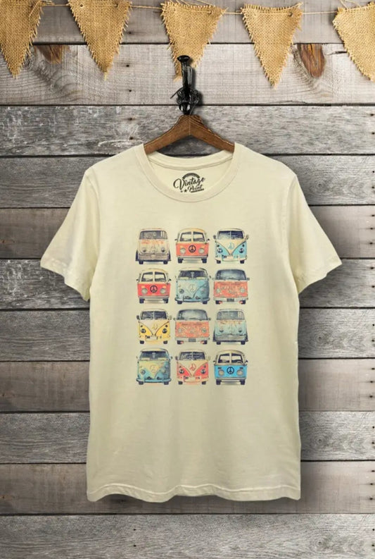 A cream-colored graphic tee with a screenprint design featuring multiple colorful VW vans, displayed on a hanger against a wooden backdrop with decorative bunting.